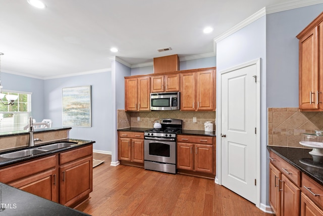 kitchen featuring visible vents, wood finished floors, brown cabinets, a sink, and appliances with stainless steel finishes