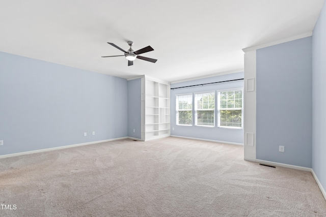 empty room featuring carpet floors, visible vents, ornamental molding, baseboards, and a ceiling fan