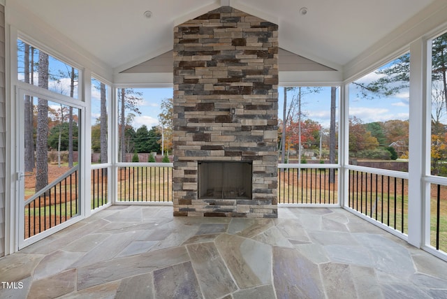 unfurnished sunroom with an outdoor stone fireplace, vaulted ceiling, and a wealth of natural light