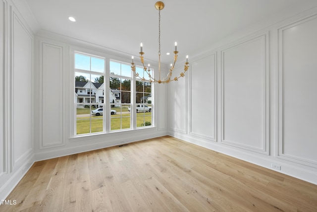 unfurnished dining area featuring a notable chandelier, light wood-type flooring, and ornamental molding