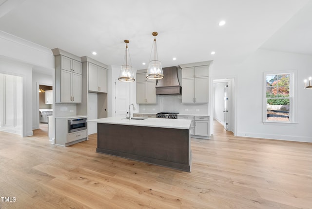 kitchen with custom exhaust hood, sink, a kitchen island with sink, and light hardwood / wood-style flooring