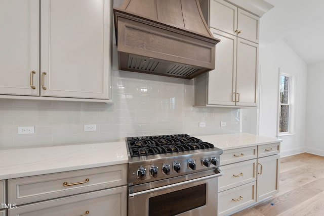 kitchen with premium range hood, high end stainless steel range oven, light hardwood / wood-style flooring, decorative backsplash, and light stone counters