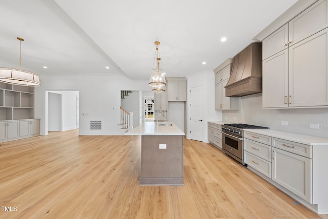 kitchen featuring pendant lighting, a kitchen island with sink, high end stainless steel range, light wood-type flooring, and custom range hood