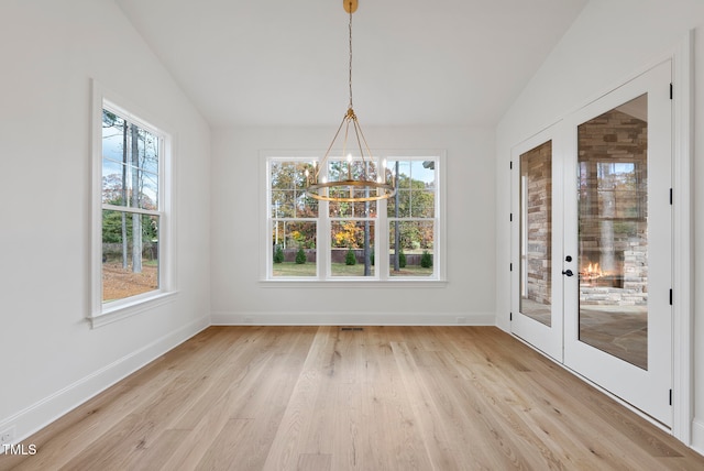 unfurnished dining area with a notable chandelier, french doors, vaulted ceiling, and light wood-type flooring