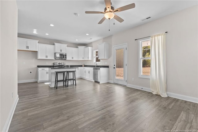 kitchen with a kitchen bar, appliances with stainless steel finishes, a kitchen island, ceiling fan, and white cabinetry