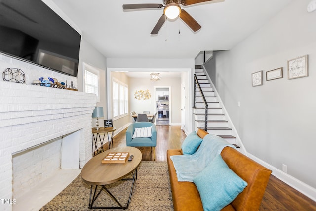 living room featuring ceiling fan, wood-type flooring, and a brick fireplace