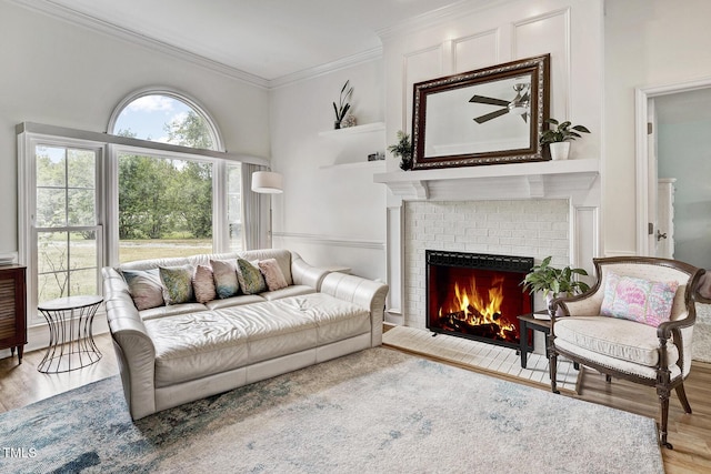 living room featuring built in shelves, ceiling fan, crown molding, light hardwood / wood-style flooring, and a fireplace