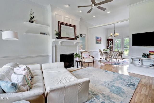 living room featuring ceiling fan with notable chandelier, a fireplace, light wood-type flooring, and ornamental molding