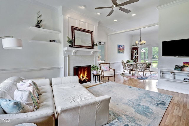 living room featuring ceiling fan with notable chandelier, light wood-type flooring, a brick fireplace, and crown molding