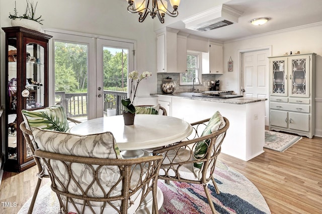 dining area featuring french doors, sink, crown molding, light hardwood / wood-style floors, and a chandelier