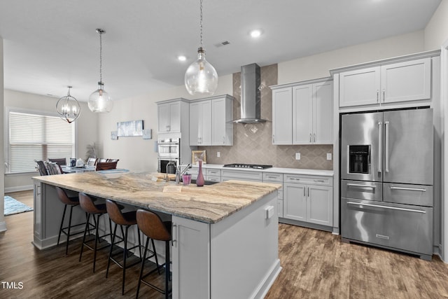 kitchen with a kitchen island with sink, stainless steel appliances, visible vents, dark wood-style floors, and wall chimney exhaust hood