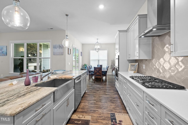 kitchen featuring stainless steel appliances, dark wood-type flooring, a sink, wall chimney range hood, and tasteful backsplash