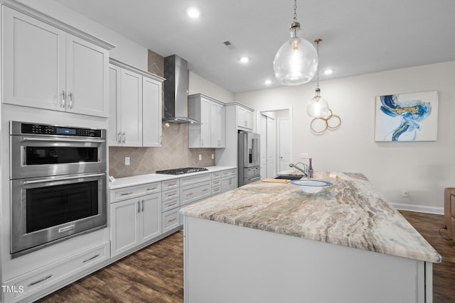 kitchen with a sink, wall chimney range hood, appliances with stainless steel finishes, decorative backsplash, and dark wood-style floors