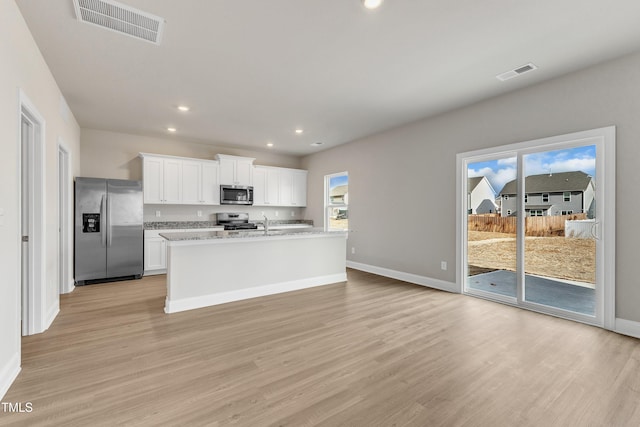 kitchen with stainless steel appliances, a center island with sink, white cabinets, and light wood-type flooring