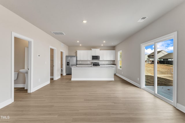 kitchen with white cabinetry, stainless steel appliances, light stone counters, light hardwood / wood-style floors, and a center island with sink