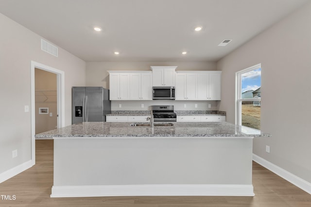 kitchen with sink, white cabinetry, stainless steel appliances, light stone counters, and a center island with sink