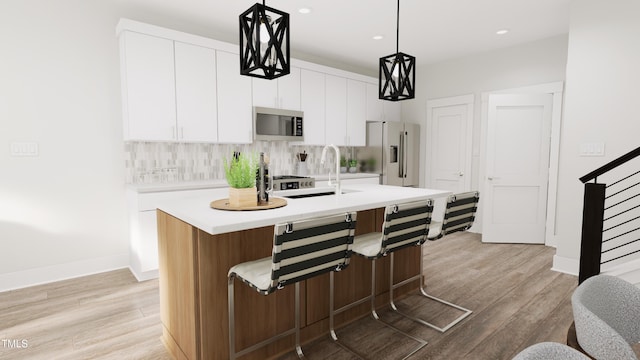 kitchen featuring stainless steel appliances, decorative backsplash, white cabinets, a center island with sink, and decorative light fixtures