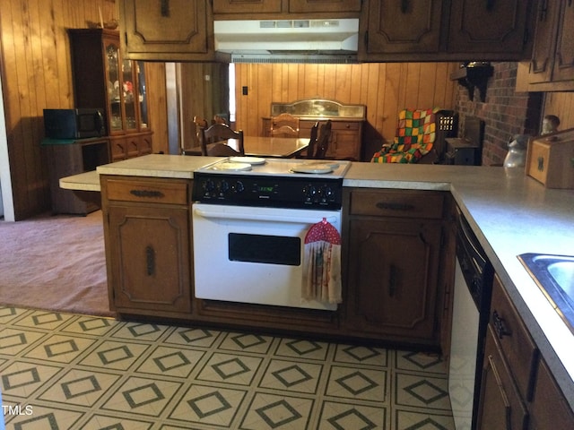 kitchen with kitchen peninsula, wooden walls, light colored carpet, and white appliances