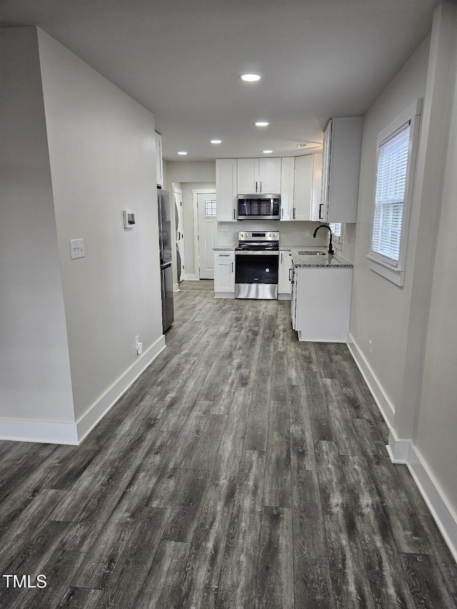 kitchen with light stone counters, stainless steel appliances, dark wood-type flooring, sink, and white cabinets