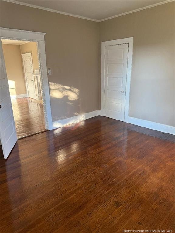 empty room with dark hardwood / wood-style floors and crown molding