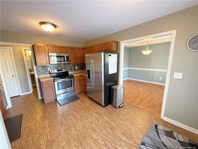 kitchen featuring decorative backsplash, appliances with stainless steel finishes, light wood-type flooring, and pendant lighting