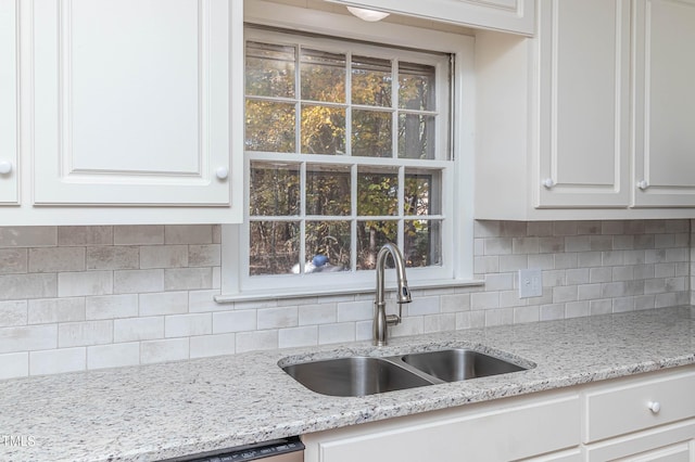 kitchen with decorative backsplash, white cabinetry, sink, and light stone countertops