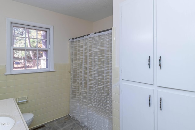 bathroom with walk in shower, a textured ceiling, toilet, vanity, and tile walls