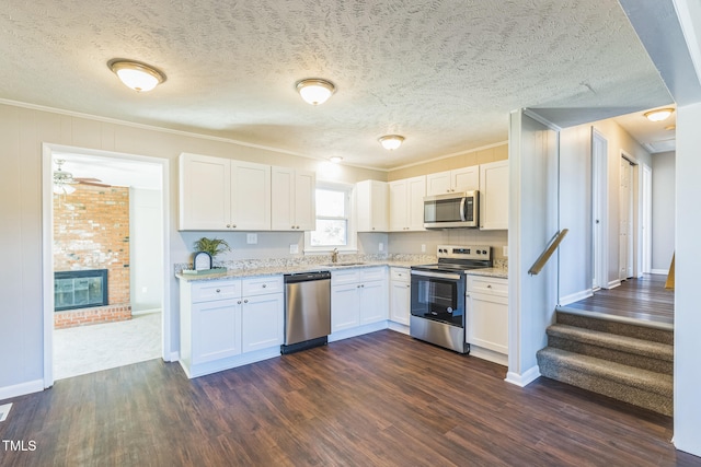 kitchen featuring a brick fireplace, stainless steel appliances, white cabinetry, and dark hardwood / wood-style floors