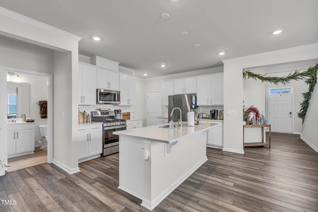 kitchen with appliances with stainless steel finishes, dark wood-type flooring, sink, white cabinetry, and an island with sink