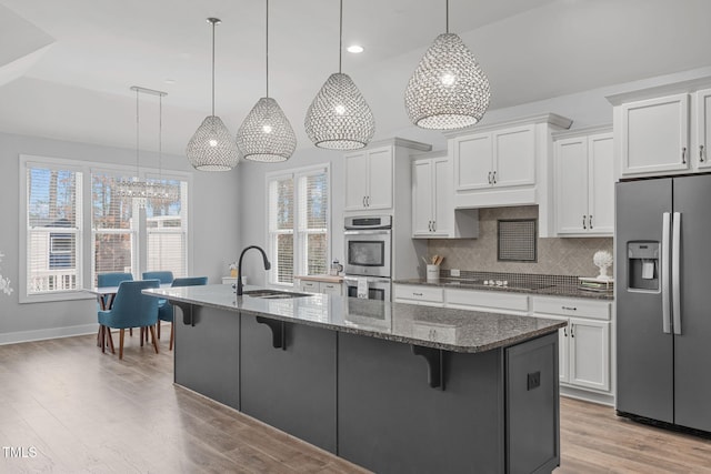 kitchen with hanging light fixtures, an island with sink, white cabinets, and appliances with stainless steel finishes