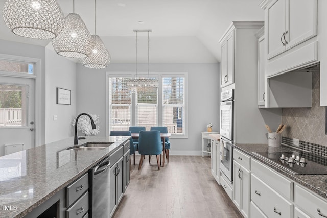 kitchen with pendant lighting, sink, dark stone countertops, white cabinets, and backsplash