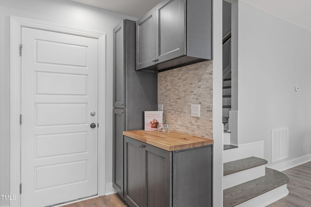 kitchen with wooden counters, gray cabinets, light wood-type flooring, and backsplash