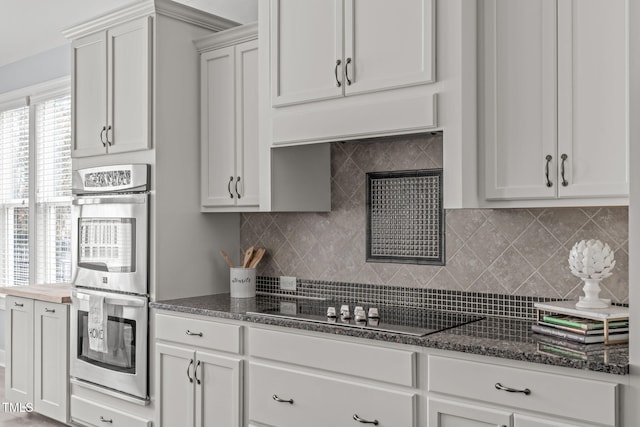 kitchen with white cabinetry, dark stone counters, decorative backsplash, stainless steel double oven, and black electric cooktop