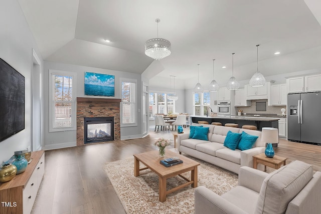 living room featuring sink, light hardwood / wood-style flooring, a stone fireplace, vaulted ceiling, and a chandelier