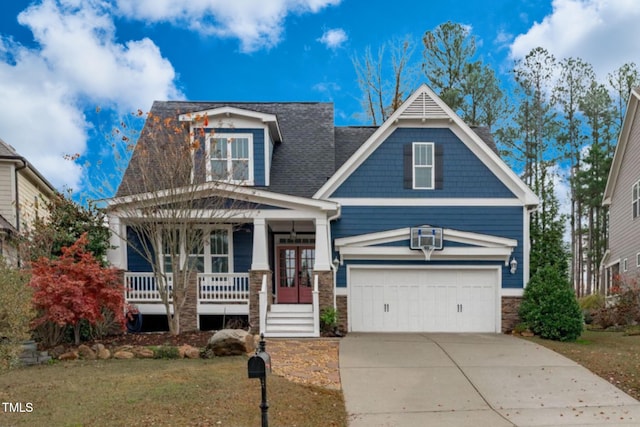 craftsman house featuring a porch, a garage, driveway, stone siding, and a front lawn