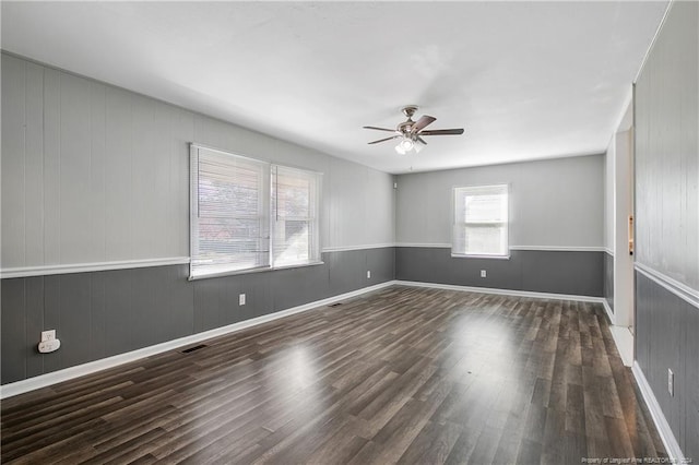 unfurnished room featuring dark hardwood / wood-style floors, a wealth of natural light, wooden walls, and ceiling fan