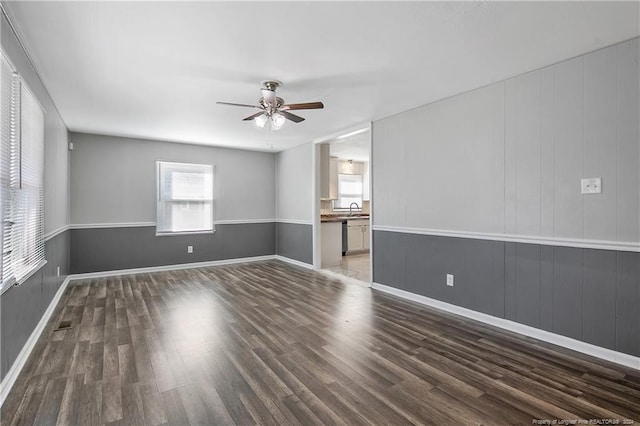 empty room with sink, dark hardwood / wood-style floors, ceiling fan, and wood walls