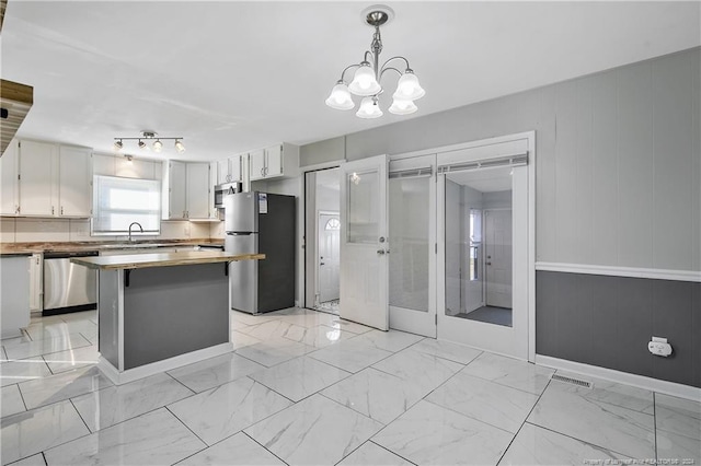 kitchen with appliances with stainless steel finishes, sink, an inviting chandelier, white cabinets, and hanging light fixtures