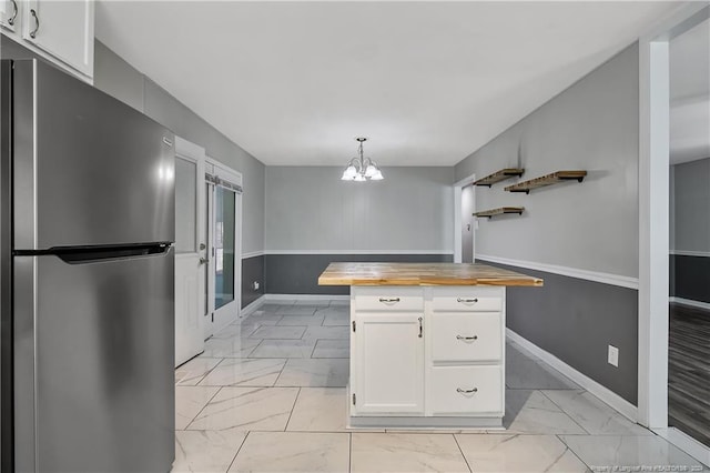 kitchen with white cabinets, stainless steel refrigerator, hanging light fixtures, and butcher block counters