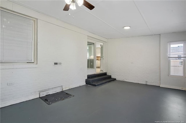 spare room featuring ceiling fan and brick wall