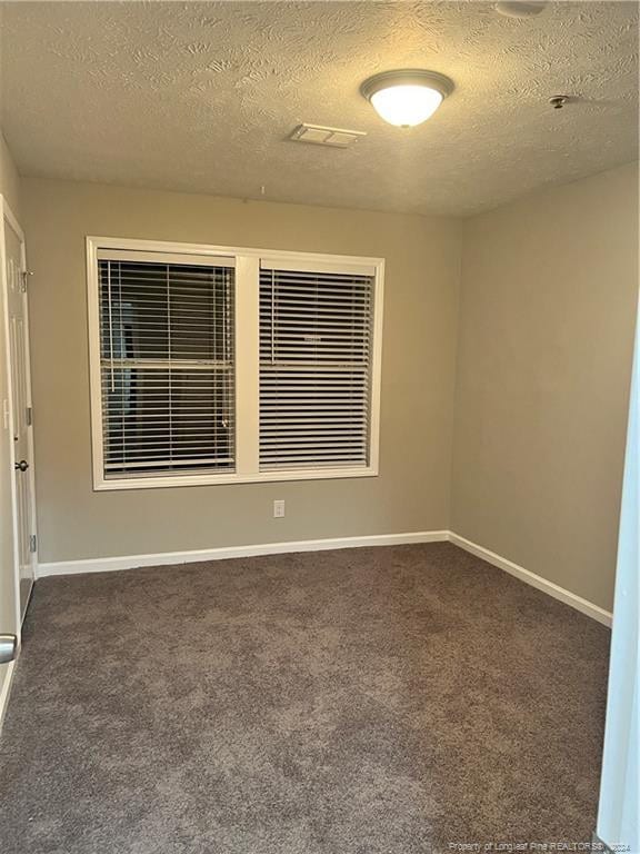 spare room featuring dark carpet and a textured ceiling