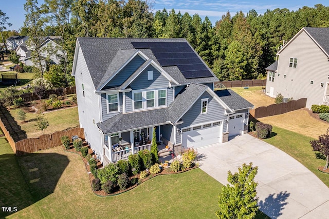 view of front of home featuring a porch, a garage, solar panels, and a front yard