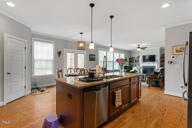 kitchen with decorative light fixtures, light wood-type flooring, light stone counters, a kitchen island with sink, and stainless steel appliances