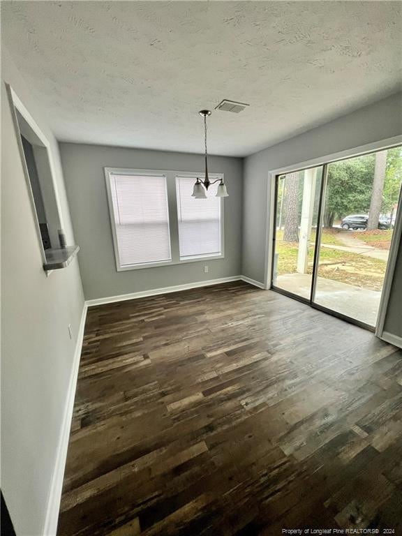 unfurnished dining area with a chandelier, a textured ceiling, and dark wood-type flooring