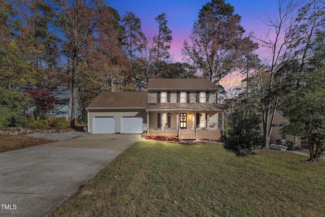 colonial home featuring a garage, covered porch, and a yard