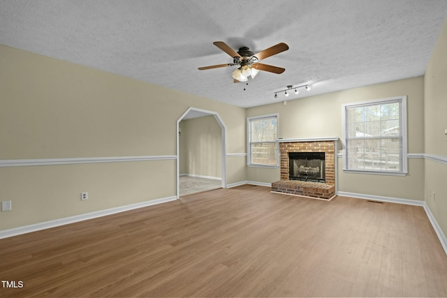 unfurnished living room with a fireplace, a textured ceiling, light hardwood / wood-style flooring, and ceiling fan