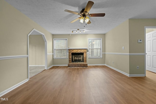 unfurnished living room featuring a fireplace, a textured ceiling, light hardwood / wood-style floors, and ceiling fan