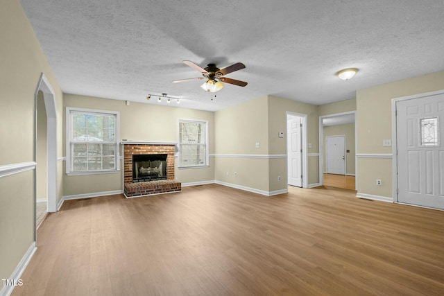 unfurnished living room featuring a textured ceiling, ceiling fan, a fireplace, and light hardwood / wood-style flooring