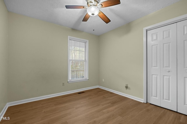 unfurnished bedroom featuring ceiling fan, a closet, a textured ceiling, and light hardwood / wood-style flooring