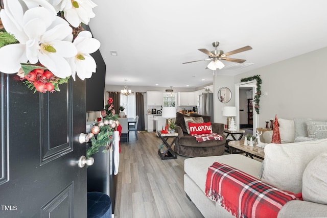 living room featuring ceiling fan with notable chandelier and light wood-type flooring